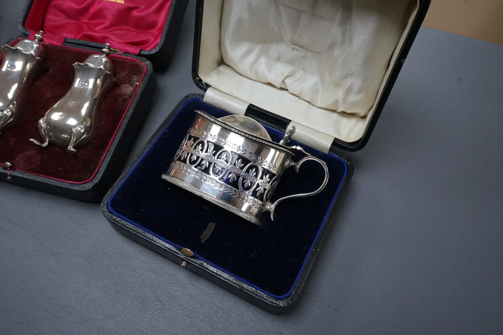 Three cased silver items including an Edwardian christening trio, a pair of George V pepperettes, Birmingham, 1916 and a George V pierced silver oval mustard pot, Birmingham, 1916.